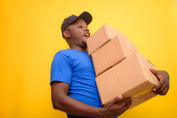 An African delivery or dispatch man with blue shirt carrying boxes and wearing a face cap
