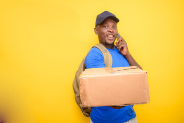 An African dispatch man with back pack, making a call, carrying boxes and wearing a face cap