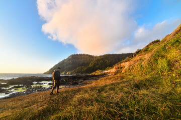 Man with backpack walking on the oceanside trail at sunset time for a camping