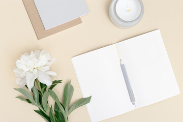 Top view of open notebook and white peony flower on table. Creative workspace minimal style with aroma candle for comfort work