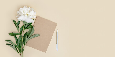 Woman workspace, closed notebook, pen, white peony flower on beige background. Work at summer time.