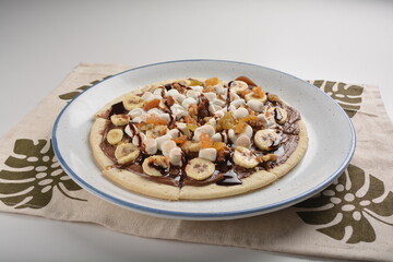 baked chocolate banana pizza with marshmallow and dry grape fruit dessert for kids in white background western halal menu
