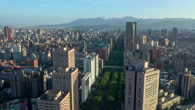 Slow aerial forward flight over green famous renai road with trees surrounded by high rise buildings and silhouette of  mountains in background. Taipei, capital of taiwan,south east asia