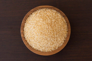 Closeup brown sugar in wooden bowl isolated on wood table background. Top view. Flat lay.