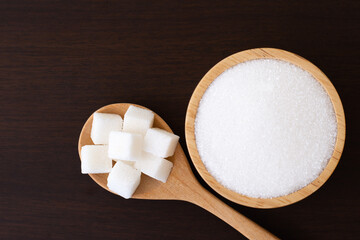 Fototapeta na wymiar White sand sugar in wooden bowl and cube sugar on dark background. 