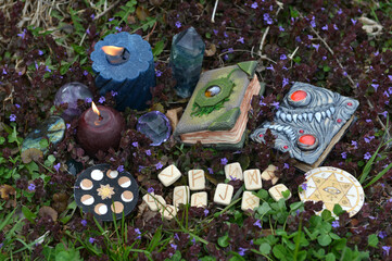 Beltane ritual still life with witch magic books, runes, crystals and burning candles outside.