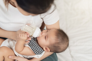 mother feeding milk from bottle and baby sleeping on bed