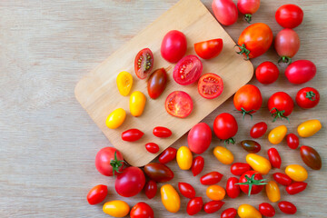 Fresh tomatoes of various colors, sizes, varieties on a wooden floor and cut in half placed on a cutting board.