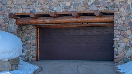 Pano Home in Park City Utah with garage door framed by stone wall and wooden logs