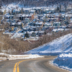 Square Scenic mountain landscape with road passing along homes on a snowy neighborhood