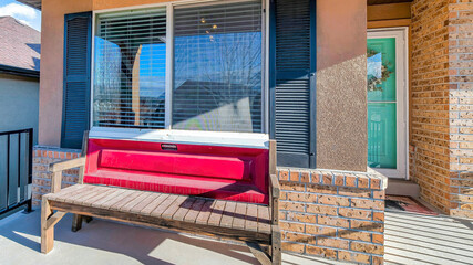 Pano Sunlit open front porch of home with wooden bench against window with shutters