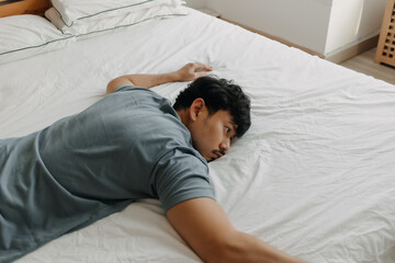 Tired Asian man is lying on the bed as he out of energy.