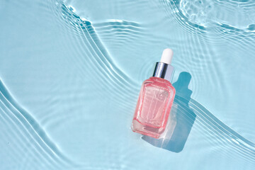 Cosmetic medical skincare, glass pink serum bottle with collagen on blue water background with waves