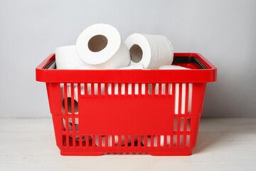 Shopping basket with rolls of toilet paper on table near light wall