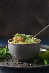 Bowl with tasty guacamole and lime on dark background, closeup