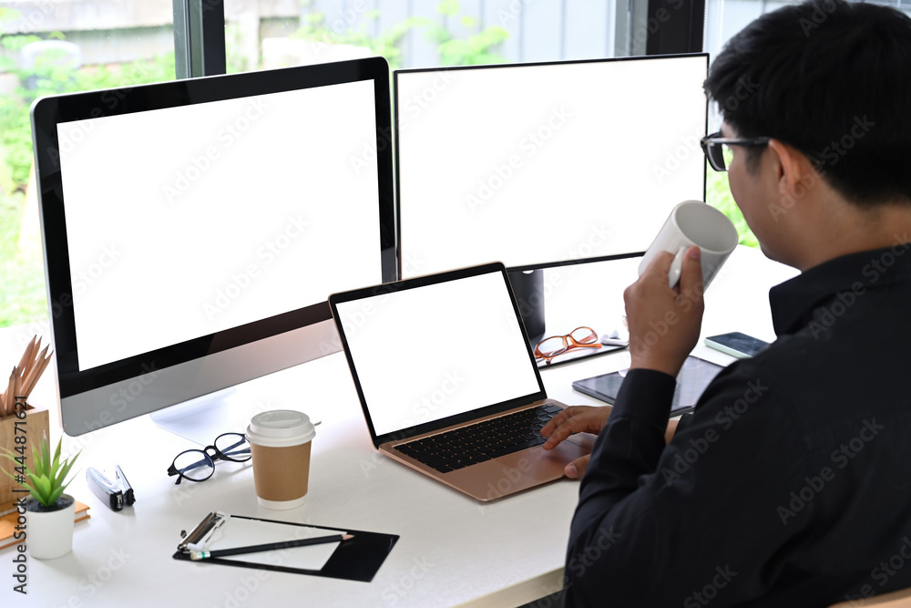Poster back view man programer drinking coffee and working in modern workplace.