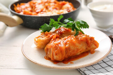 Plate with tasty stuffed cabbage rolls on light wooden background