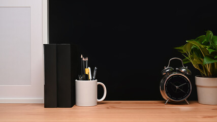 Picture frame, houseplant, books and alarm clock on wooden table.