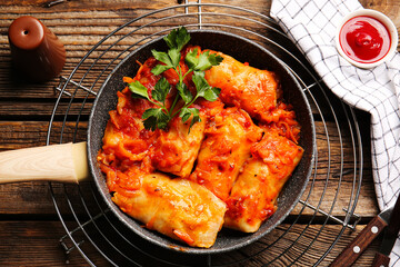 Frying pan with tasty stuffed cabbage rolls on wooden background