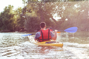 Man paddles a yellow kayak on the Danube river in the rays of the sun at summer season