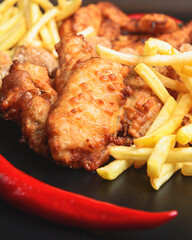 Hot spicy deep fried set. Deep fried chicken, cheese camembert and french fries over black background.