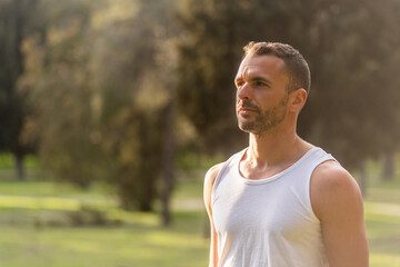 Close-up of an adult man wearing white top tank looking away in the park