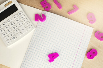 An open notebook in a cage with a white calculator lies on a wooden table against the background of illumination. Educational and business concept