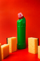 green bottle with cleaning agent and cleaning sponges on a red background