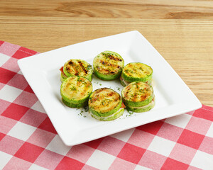 Appetizer from tomatoes, zucchini and mozzarella cheese served on a white plate over red plaid tablecloth.