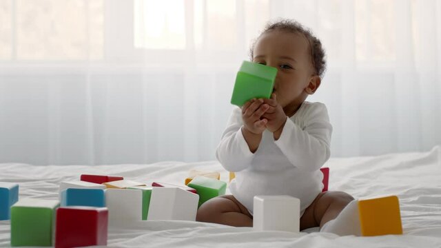 Cute little curly african american baby boy playing with colorful blocks, sitting on bed, tracking shot, slow motion