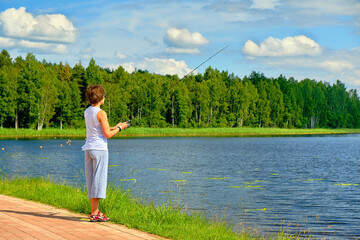 woman fishing on a spinning rod in the lake on summer day