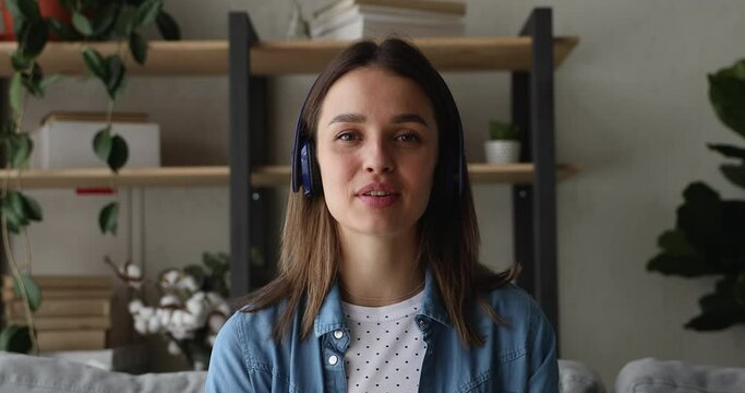 Happy millennial generation attractive woman wearing headphones looking at camera, enjoying pleasant conversation by video call application, talking speaking chatting sharing life news distantly.