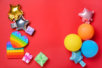 Pop it fidget toys, balloons and gifts on color background