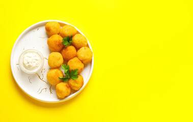 Plate with fried potato balls and sauce on color background