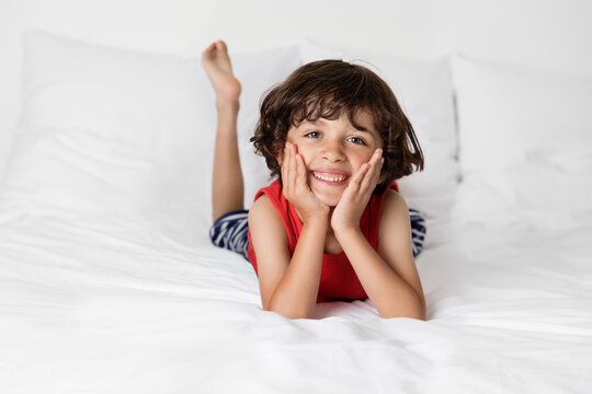 Smiling young boy lying on white bed with chin on hands