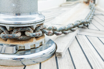 Part of a teak deck on a yacht with a stainless steel winch and an anchor chain attachment mechanism, close-up.