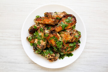 Home-baked Garlic Parmesan Chicken Wings on a white plate on a white wooden background, top view. Flat lay, overhead, from above.