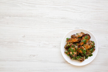 Homemade baked Garlic Parmesan Chicken Wings on a white plate on a white wooden background, top view. Flat lay, overhead, from above. Copy space.