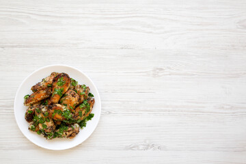 Homemade baked Garlic Parmesan Chicken Wings on a white plate on a white wooden background, top view. Flat lay, overhead, from above. Copy space.
