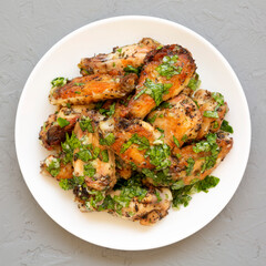 Homemade baked Garlic Parmesan Chicken Wings on a white plate on a gray background, top view. Flat lay, overhead, from above.