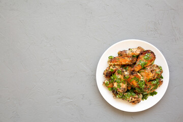 Homemade baked Garlic Parmesan Chicken Wings on a white plate on a gray background, top view. Flat lay, overhead, from above. Space for text.