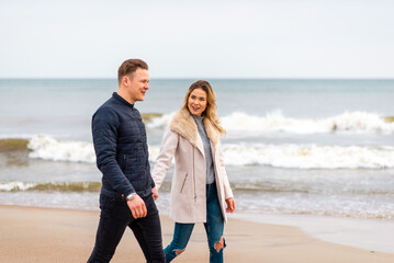 Attractive young couple walking along the shore of a sandy beach, on a spring romantic holiday,...