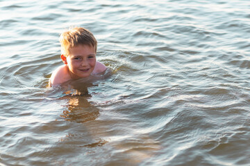Fototapeta na wymiar Happy smiling boy having fun swimming in the water.Cute boy swimming in water. Summer vacation.