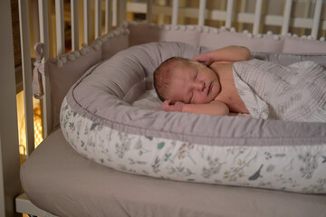 A baby newborn is sleeping in a baby cocoon with a burning night light. A child is an infant in a...