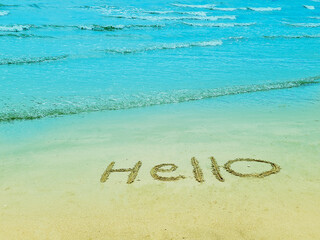 Handwritten hello message on sandy beach and clear sea