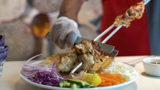 kebab on skewers served on a plate with pita bread and salads 