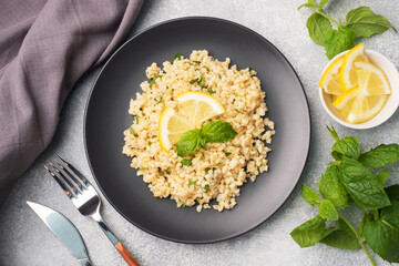 Boiled bulgur with fresh lemon and mint on a plate. A traditional oriental dish called Tabouleh. Gray concrete background