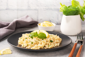 Boiled bulgur with fresh lemon and mint on a plate. A traditional oriental dish called Tabouleh. Gray concrete background