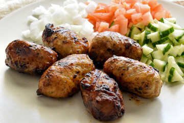 Sheftalia : Cypriot Lamb and Pork Sausages.  Grilled Sausages with Fresh Vegetables (Cucumber, Tomato Onion) on a White Plate. Traditional Cypriot food.