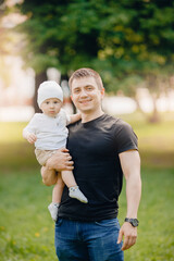 Fototapeta premium Portrait happy child boy sitting on neck of young dad, against background in park. Concept parenting and communication fathers and children.